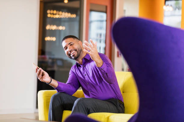 Mixed race man working in brightly colored office A mid adult mixed race Hispanic and African-American man in his 30s with short hair, a beard and mustache, sitting on a yellow sofa, holding a mobile phone. He is a businessman, perhaps a design professional, marketer or entrepreneur. beckoning stock pictures, royalty-free photos & images