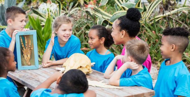 Color photo of a group of nine little kids sitting on a picnic table.