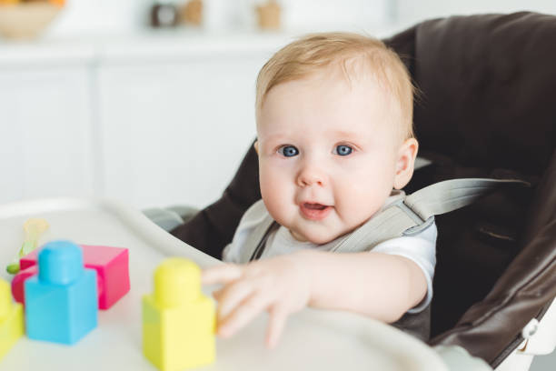 istock Smiling infant sitting in baby chair and playing with plastic blocks 949471300