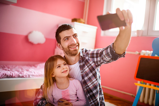 Young father and his daughter posing for a selfie image at home.
