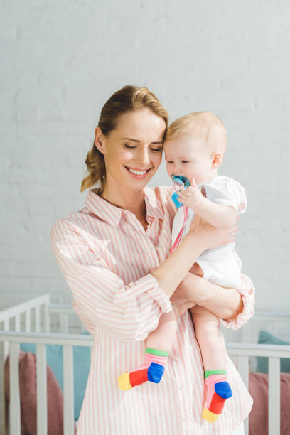 istock Smiling mother holding infant daughter with baby dummy 949481240