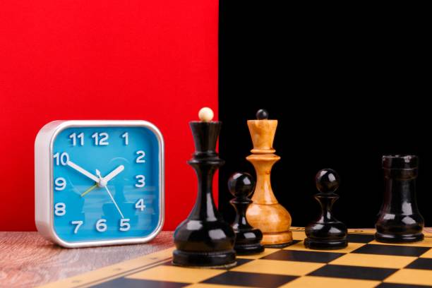 istock Blue alarm clock and chess pieces placed on the chessboard on red and black background 949485822