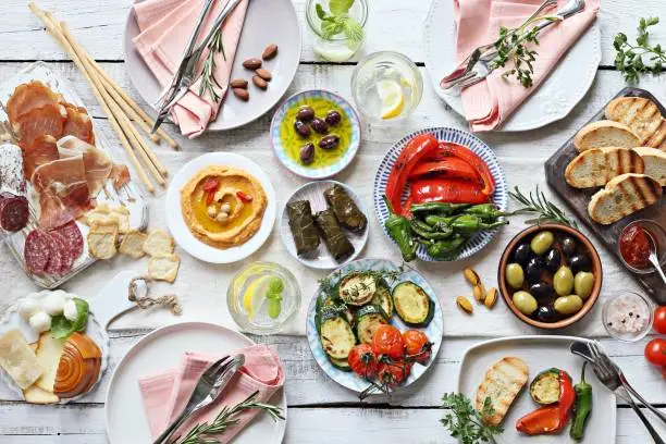 Mediterranean appetizers table concept. Diner table with antipasto selection: grilled vegetables, cured meat and salami,  jamon, olives, cheese, hummus and roasted bread.  Overhead view.