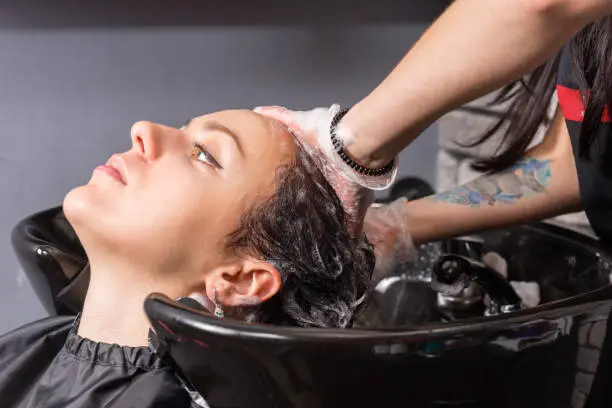 Photo of Close up profile view of young brunette woman having hair washed and soaped by stylist