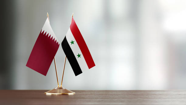 istock Qatari And Syrian Flag Pair On A Desk Over Defocused Background 949500838