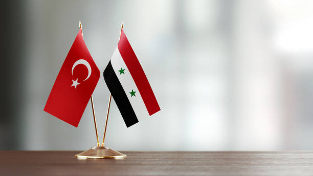 Turkish And Syrian Flag Pair On A Desk Over Defocused Background Turkish and Syrian flag pair on desk over defocused background. Horizontal composition with copy space and selective focus. syria stock pictures, royalty-free photos & images