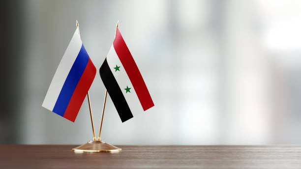 istock Russian And Syrian Flag Pair On A Desk Over Defocused Background 949503360