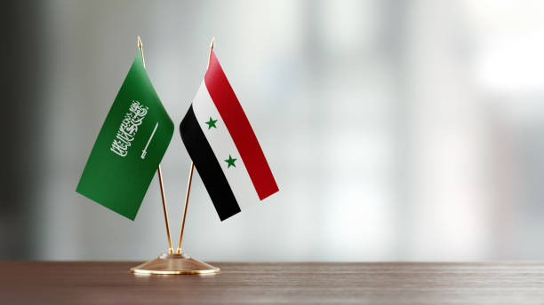 istock Saudi Arabian And Syrian Flag Pair On A Desk Over Defocused Background 949503482