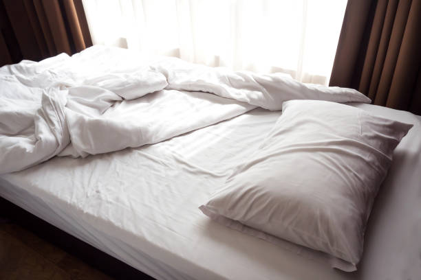 istock Messy bed. White pillow and blanket with sunlight through window. 949530168