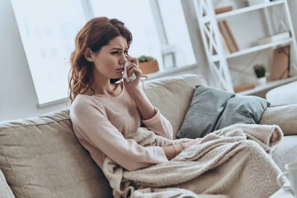 Young lonely women covered with blanket crying while sitting on the sofa at home