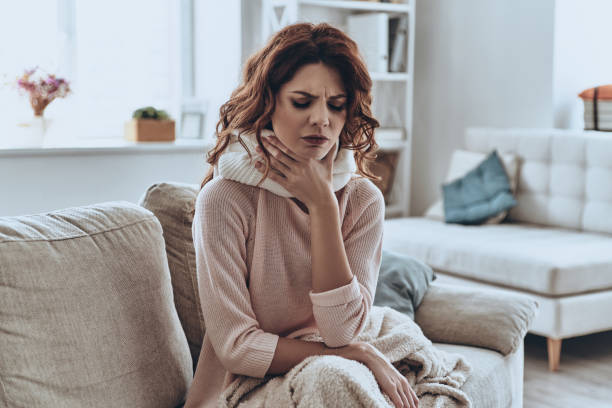 Being ill. Sick young women covered with blanket coughing while sitting on the sofa at home neck photos stock pictures, royalty-free photos & images