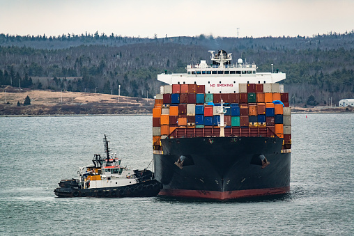 Container ship navigates Halifax Harbour with the assistance of tugboats.