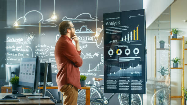 istock Marketer Looks at Interactive Touchscreen Whiteboard Showing Latest Graphs and Charts on Statistical Growth. He Works in the Creative Office. 949561062