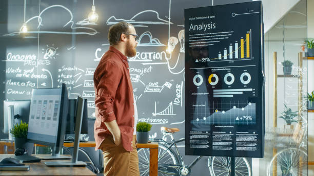istock Marketer Looks at Interactive Touchscreen Whiteboard Showing Latest Graphs and Charts on Statistical Growth. He Works in the Creative Office. 949561064