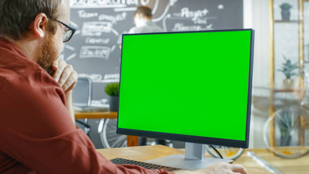 istock Man Works on the Personal Computer with Green Mock-up Screen. In the background Creative Office with Man Drawing on Chalkboard Wall. 949561096