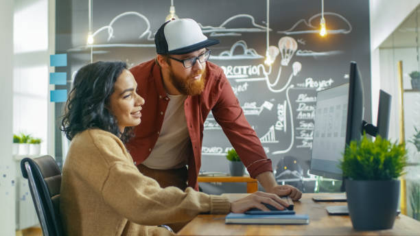 istock At the Desk Beautiful Woman Developer Talks With Programer, Together They Design New Mobile Game/ Application. They Work in the Stylish Indie Creative Studio. 949561126