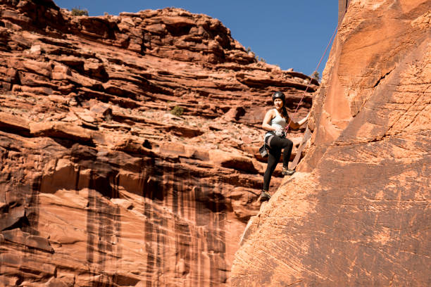 Young cute Female Climber makes difficult Move leading multi pitch route on colourful orange rocky Wall
