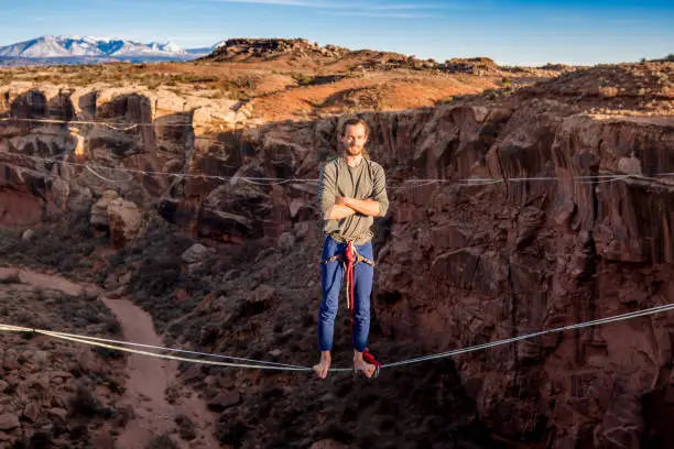 Young male extreme athlete on doing highlining or slacklining across a deep canyon near Moab Utah