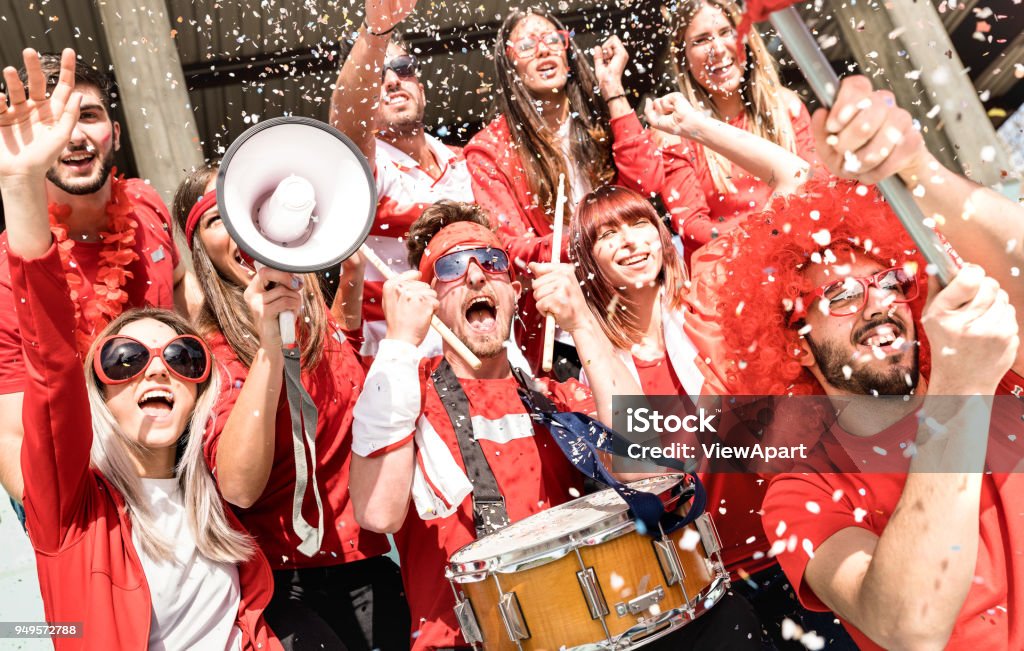 Young football supporter fans cheering with flag and confetti watching soccer match at stadium - Friends people group with red t-shirts having excited fun on sport world championship concept Soccer Stock Photo