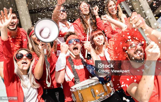 Young Football Supporter Fans Cheering With Flag And Confetti Watching Soccer Match At Stadium Friends People Group With Red Tshirts Having Excited Fun On Sport World Championship Concept Stock Photo - Download Image Now