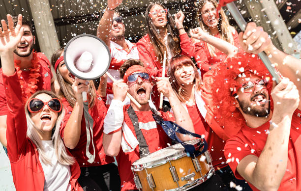 young football supporter fans cheering with flag and confetti watching soccer match at stadium - friends people group with red t-shirts having excited fun on sport world championship concept - sports event imagens e fotografias de stock