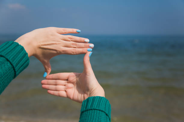 Closeup of female caucasian hands isolated on blue background. Young woman forming frame with her two hands as if looking at something virtual and invisible in sea.