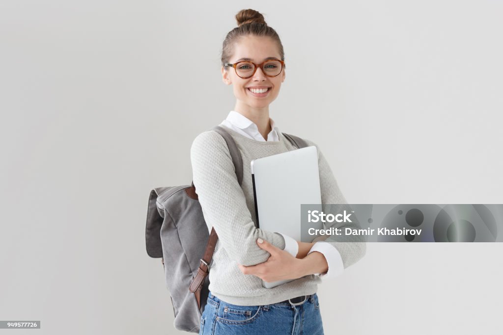 大学の学生の女の子灰色の背景に分離の研究に行く準備ができてのバックパックを身に着けている、胸にラップトップを押すと、カメラで笑顔の屋内の写真は、新しいプロジェクトを開始し� - 学生のロイヤリティフリーストックフォト