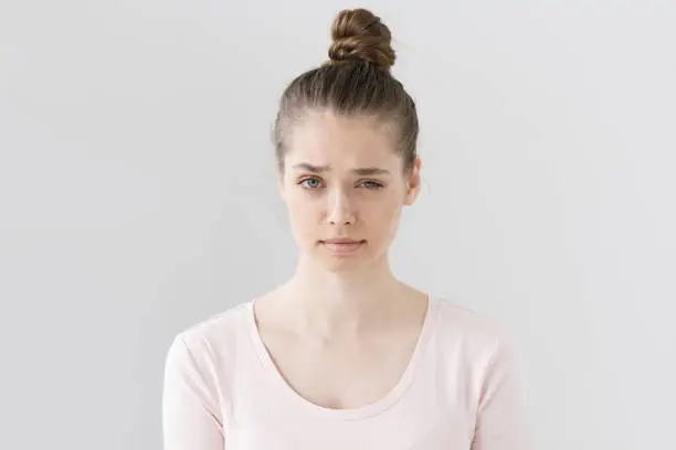 Closeup picture of nice young female without make up isolated on grey background raising eyebrow with vivid expression of suspicion, looking mistrustful towards she is hearing and looking at.