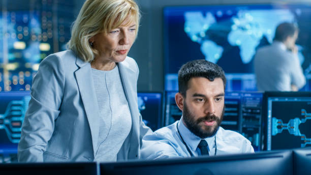 istock In the System Control Room Senior Technical Supervisor Observes Work of the Operator. In the Background People Working and Monitors Showing Relevant Technical Data. 949581004