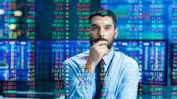 istock Stock Market Top Trader Looks at Projected Ticker Numbers and Graphs Running, Analysing Data to Make Best Sell. Behind Him Room Full of Screens and Statistics. 949581184