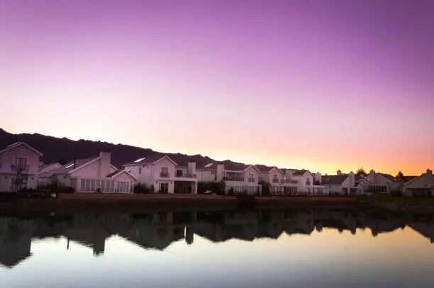 A row of houses surrounding a lake filled with reflections of the houses at sunrise, Val de Vie, Cape Town, South Africa