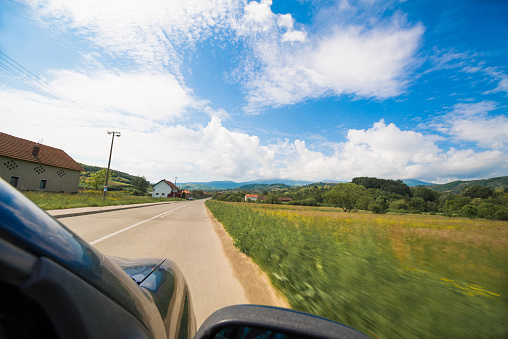 View of a car and a road during drive through a countryside on a sunny springtime day. Motion blur adds to the feeling of movement.