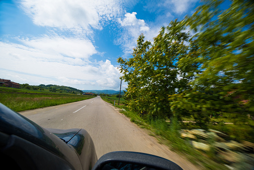 View of a car and a road during drive through a countryside on a sunny springtime day. Motion blur adds to the feeling of movement.