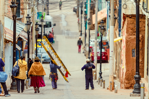 Puno, Peru - February 7, 2018: Two women walking down a street in Puno towards Lake Titicaca while a technician loads a ladder