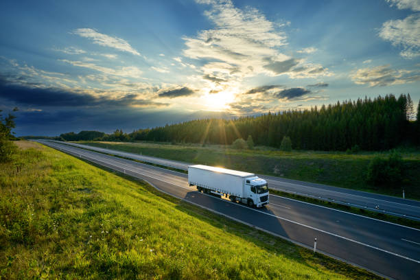 white truck driving on the highway in the countryside in the rays of the sunset with dramatic clouds - woods forest tree tree area imagens e fotografias de stock