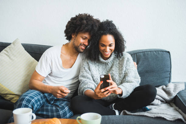 istock Couple using smart phone and smiling on the sofa 949608554