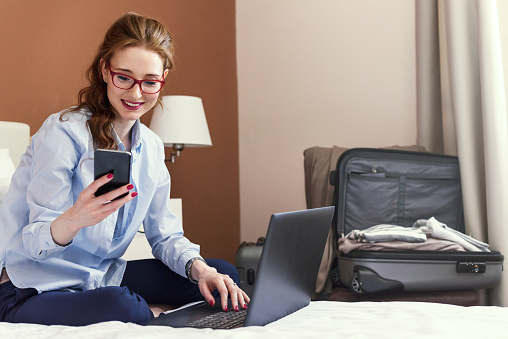 Businesswoman sitting on bed, using laptop. Woman working in hotel room. Business lady went to business trip and stayed at the hotel.