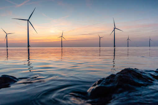 Romantic atmospheric sunset over the largest lake in the Netherlands (Ijsselmeer). Modern windmills stand in the water in a wind farm with a view from the dike and the basalt blocks of water protection.