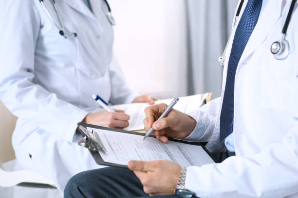 istock Two unknown doctors filling up medical form on clipboard, just hands closeup. Physicians asking question to patient or discussing medication program. Healthcare, insurance and medicine concept 949618644