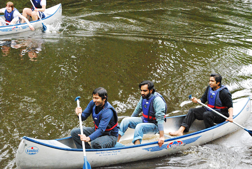 Three Asian students struggle to paddle on during student summer event competition at the Mid Sweden University, Sundsvall, Sweden. Other competitors at the background