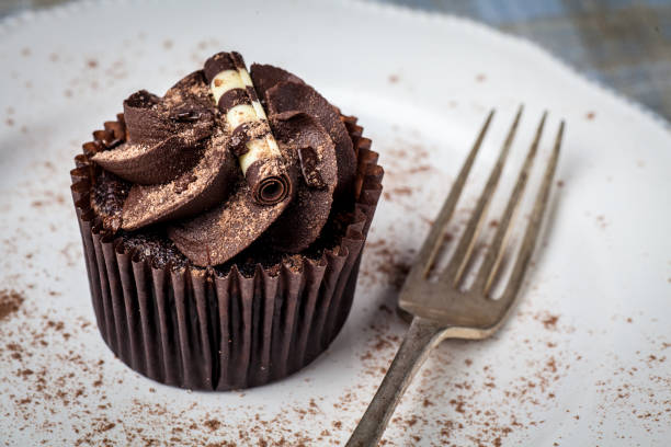 istock Chocolate cupcake on white plate with fork, dusted with cocoa powder 949627226