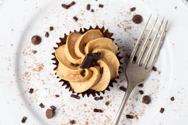 istock Salted Caramel cupcake on white plate with fork, dusted with cocoa powder and chocolate sprinkles, Overhead View 949627232
