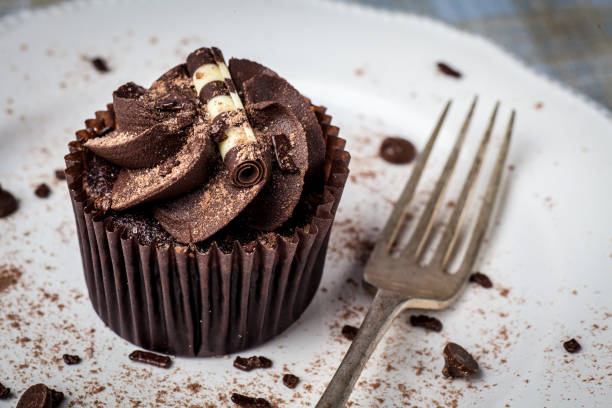 istock Chocolate cupcake on white plate with fork, dusted with cocoa powder and chocolate sprinkles 949627252