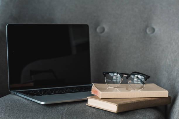 istock Laptop with empty screen and books lying on grey chair 949638820