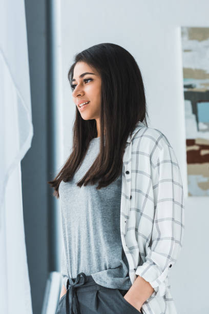 istock Attractive smiling girl standing and looking in window 949640902