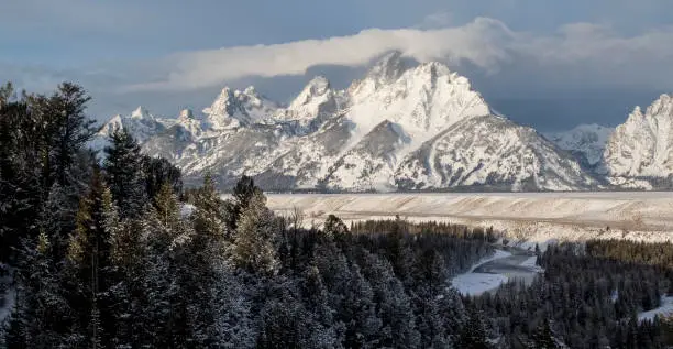 mountain range rises above a river, forest, and plains on a winter morning in Grand Teton  National Park in Jackson Hole, Wyoming