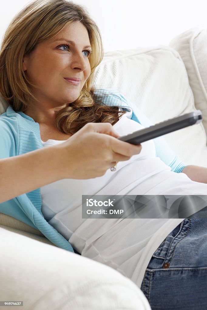 Молодая женщина расслабляющий на диване с ТВ пульт на дому - Стоковые фото Белый роялти-фри