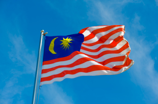 Malaysia flag tied to a pole waving against the blue sky and clouds.