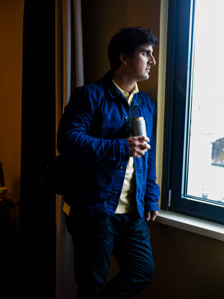 istock Man with blue jacket holding a beer near a window with beautiful light 949748352