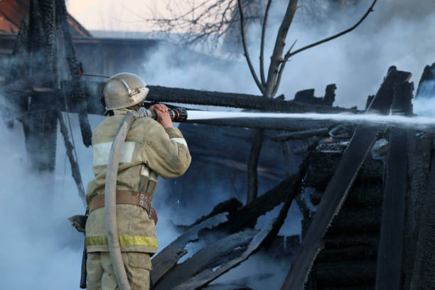 istock Firefighter extinguishes the fire. Fireman holding a hose with water, watering a strong stream of burning wooden structure in the smoke. 949816804